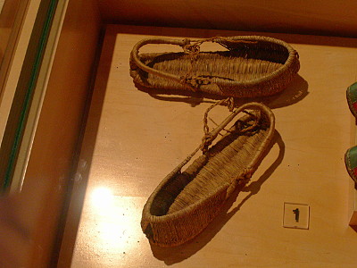 [Shoes woven of straw. The back of the shoe has a rail for the ankle. The front end of tee shoe is open top, but has full sides.]